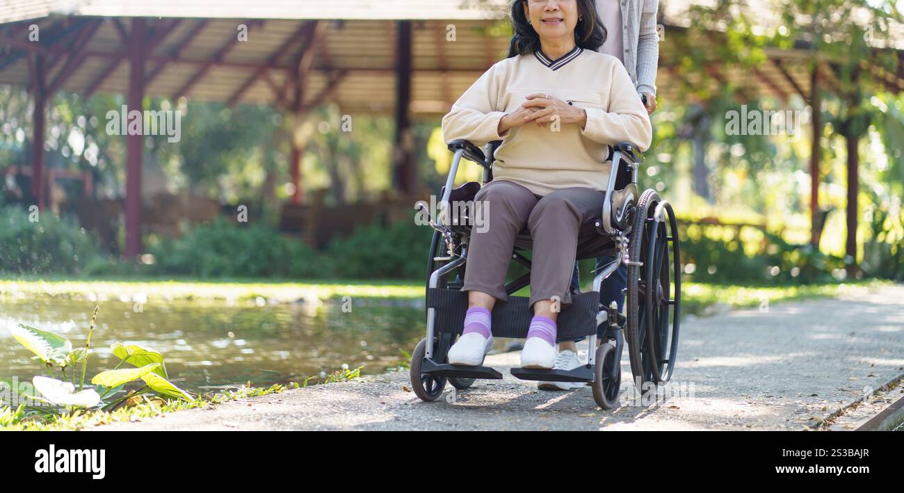 Asian senior woman in wheelchair with happy daughter. Family relationship retired woman sitting on wheelchair in the park age care at retirement home Stock Photo