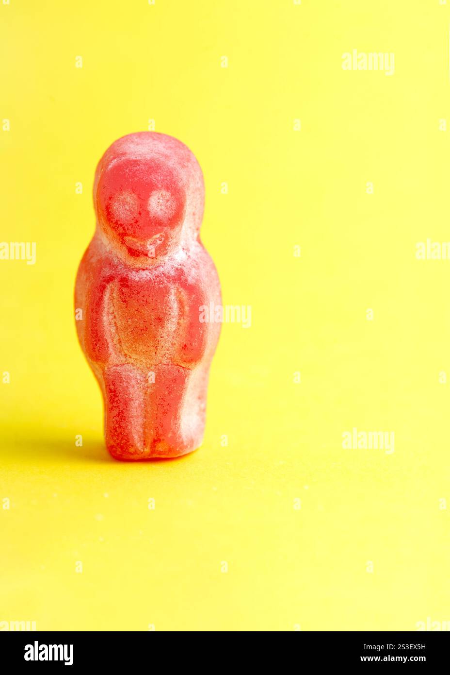 red candy figure stands alone on a vibrant yellow background, showcasing contrast, texture, and playful simplicity. concepts  isolation Stock Photo