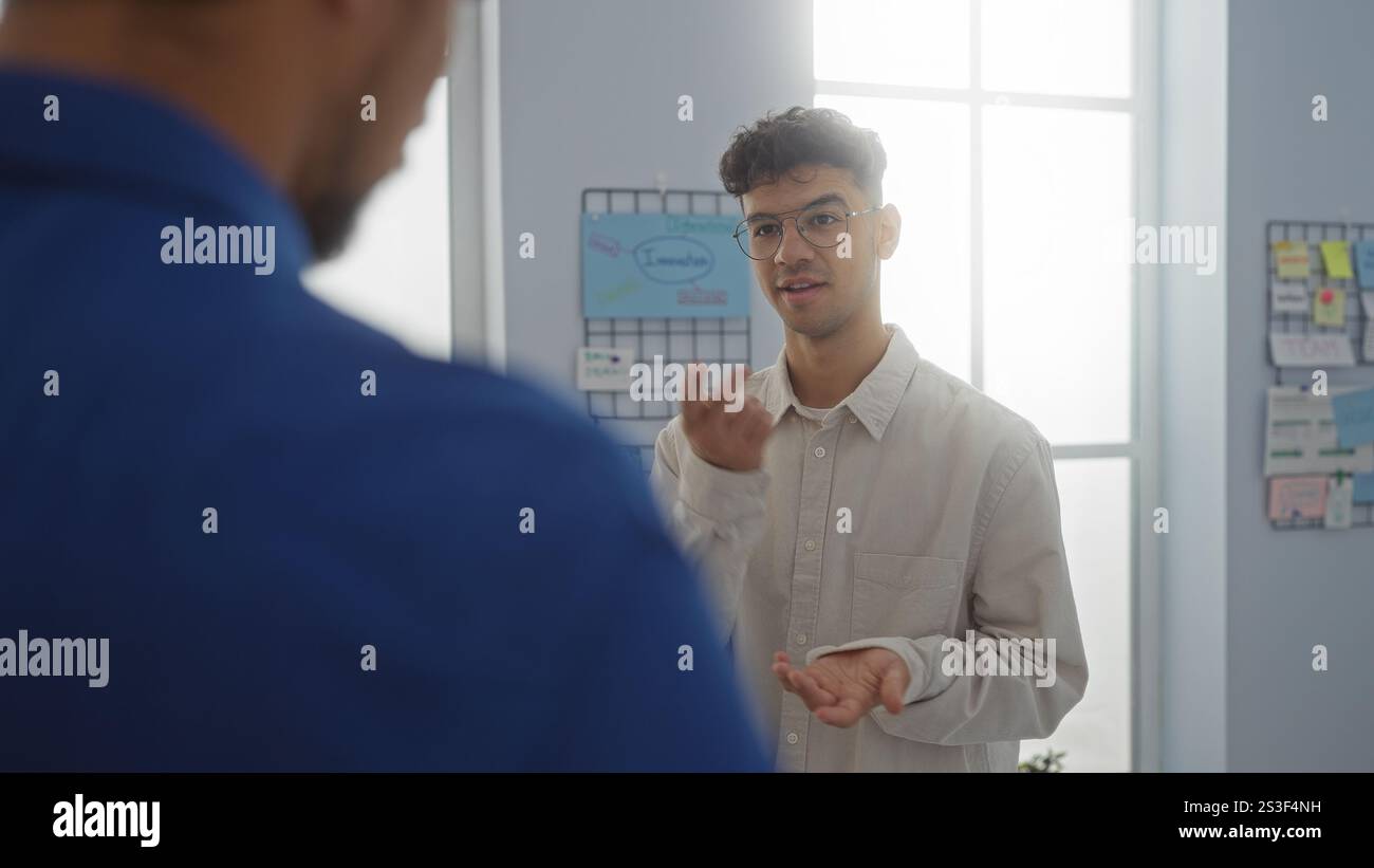 Two men discussing business in an office room with one man gesturing while the other listens attentively Stock Photo