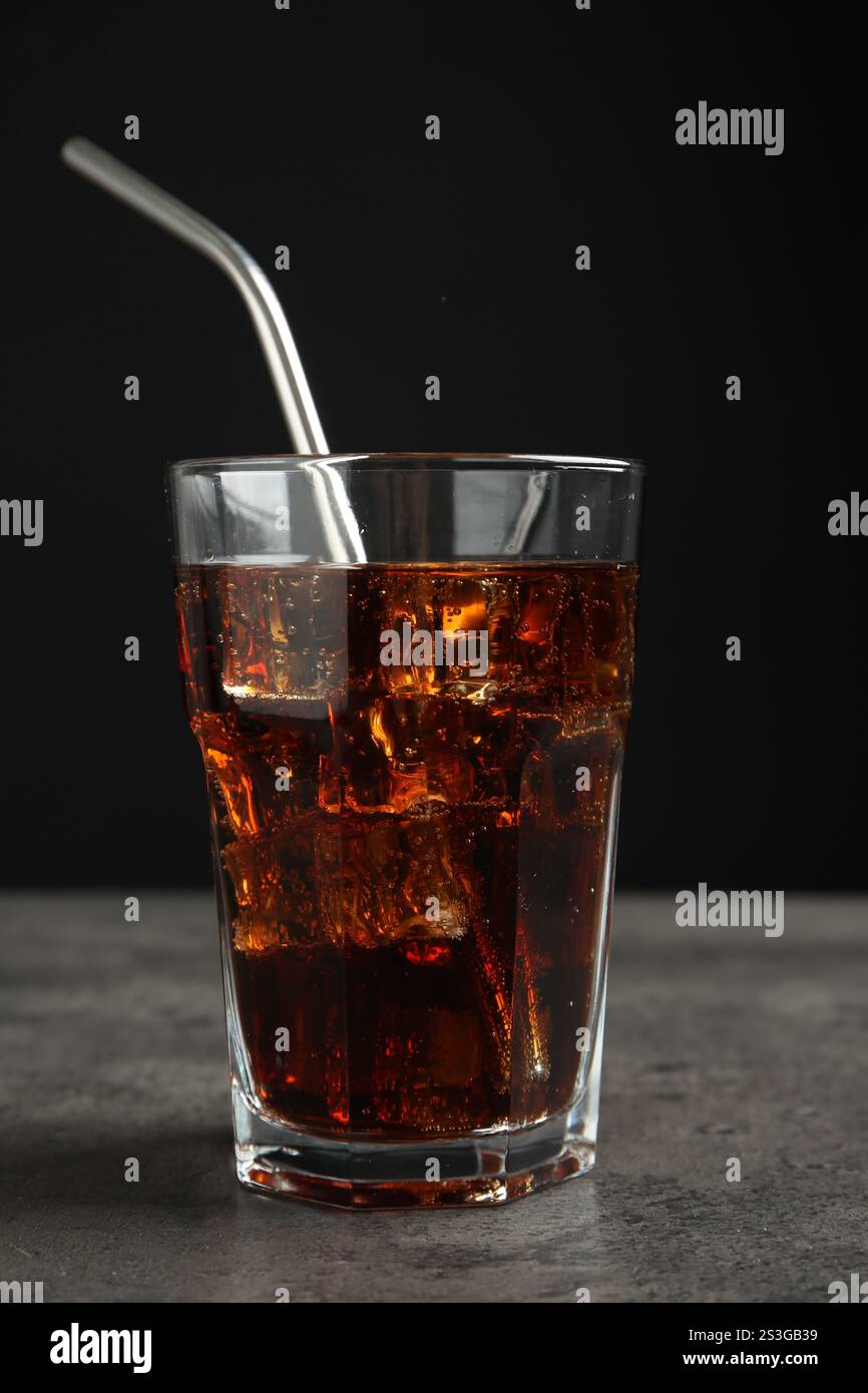 Cold cola with ice cubes and drinking straw in glass on grey table ...