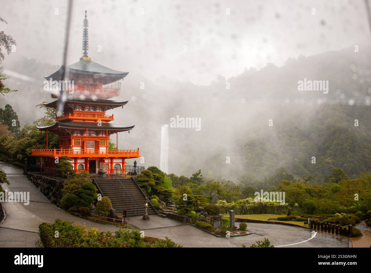Nachisan Seiganto-ji Temple pagoda with Nachi Waterfall behind in the rain from underneath an umbrella, April, Japan Stock Photo