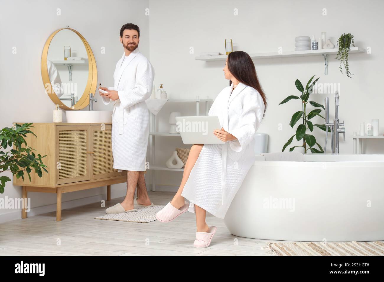 Handsome man brushing teeth while his wife using laptop in bathroom Stock Photo