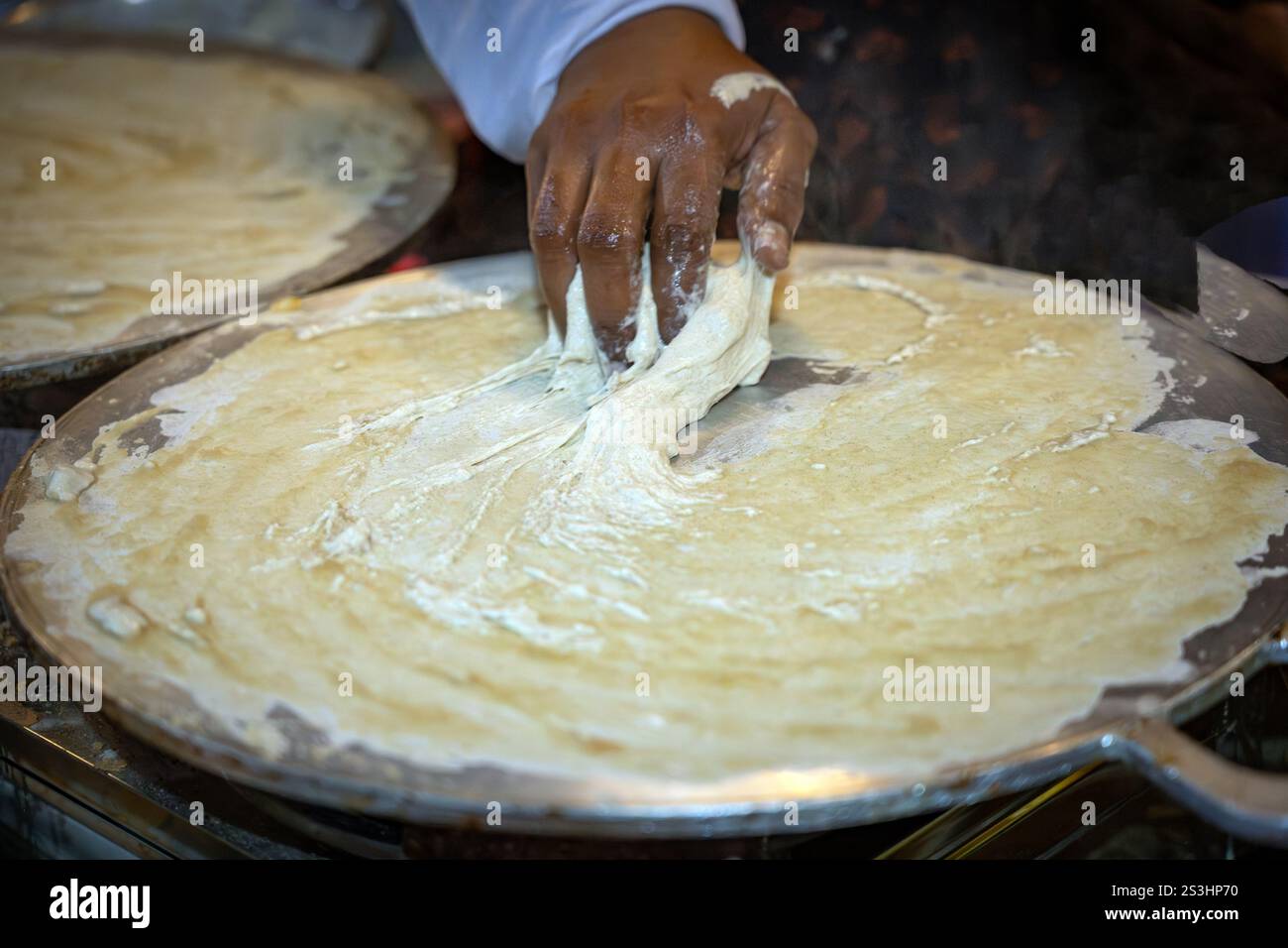 A chef skillfully spreads butter on Omani bread, known as Kuboos, over a hot griddle. This traditional delicacy is a staple of Omani cuisine, made wit Stock Photo