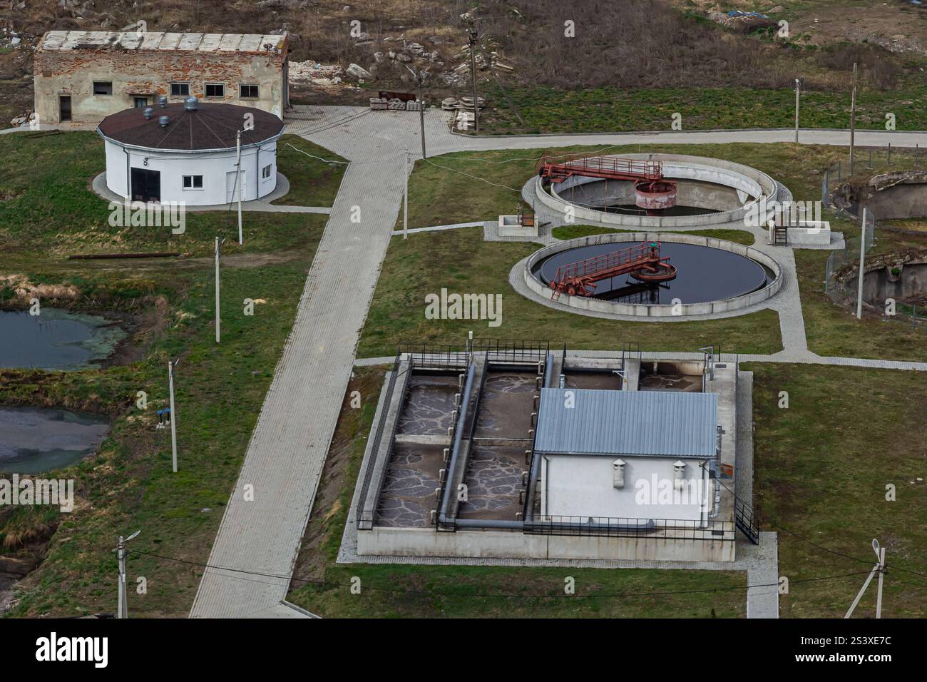 A wastewater treatment facility located in a rural setting features circular tanks for filtration and processing buildings. Green spaces surround the Stock Photo