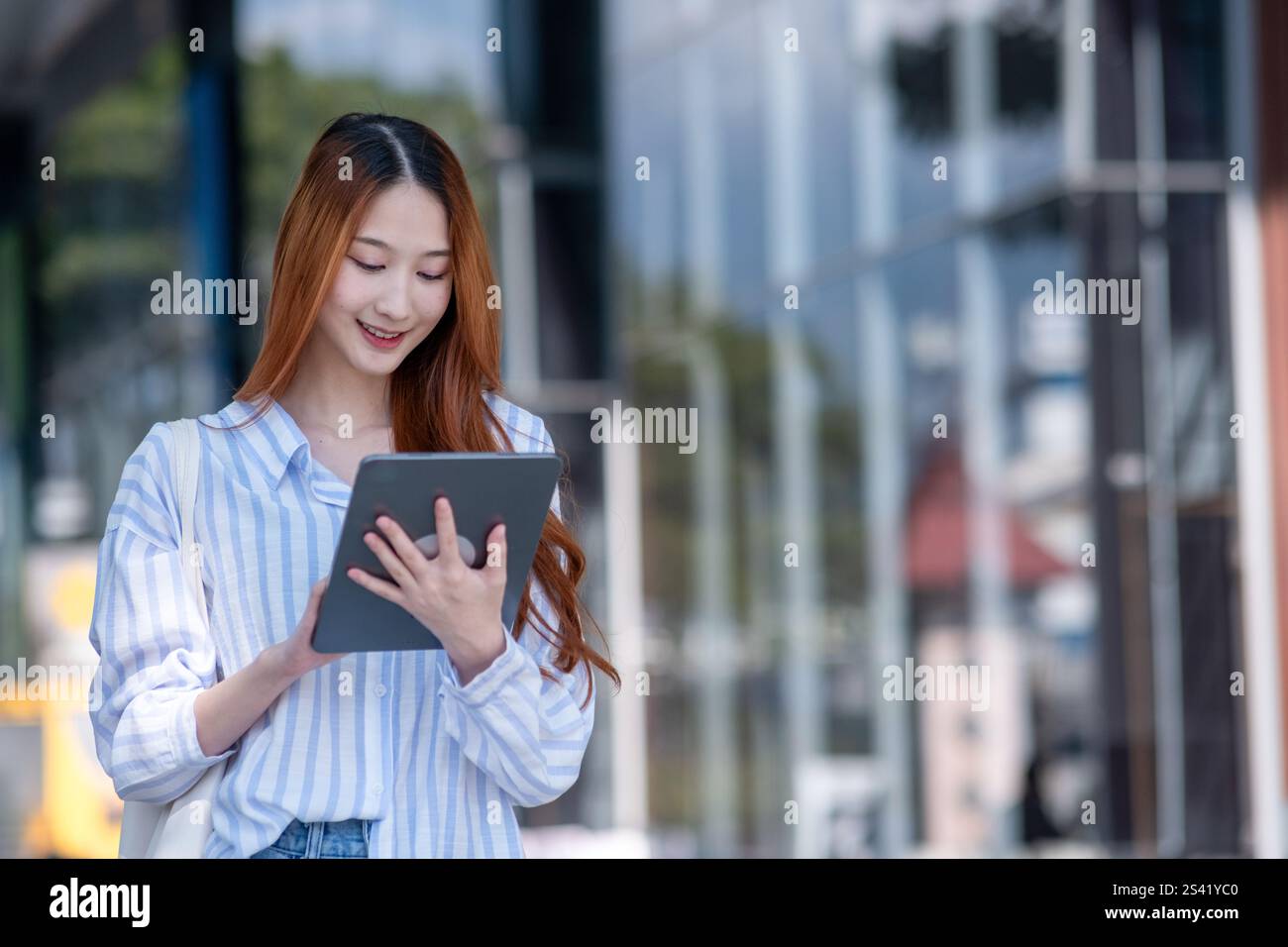 Woman is holding a tablet in her hand. She is smiling and looking at the screen Stock Photo