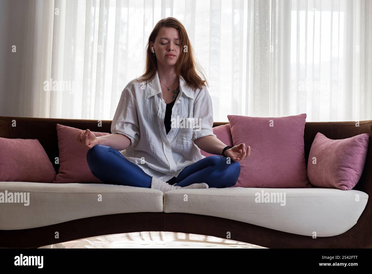 Young woman meditating on couch at home Stock Photo