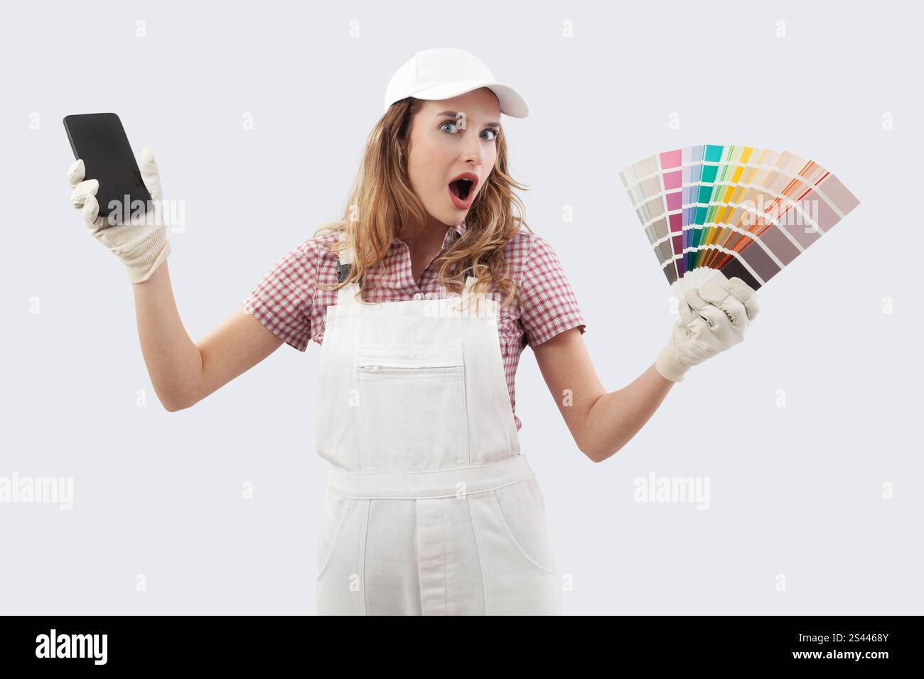 Amazed Woman in painters overalls showing phone and paint samples for ...