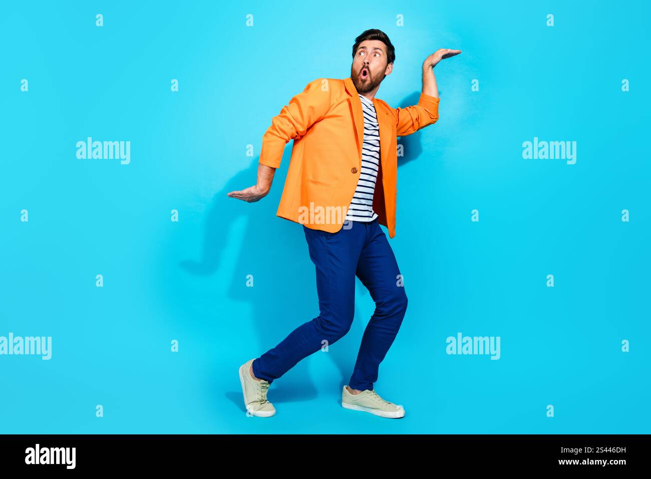 Charismatic young man in vibrant orange jacket striking a playful pose against a vibrant teal background Stock Photo