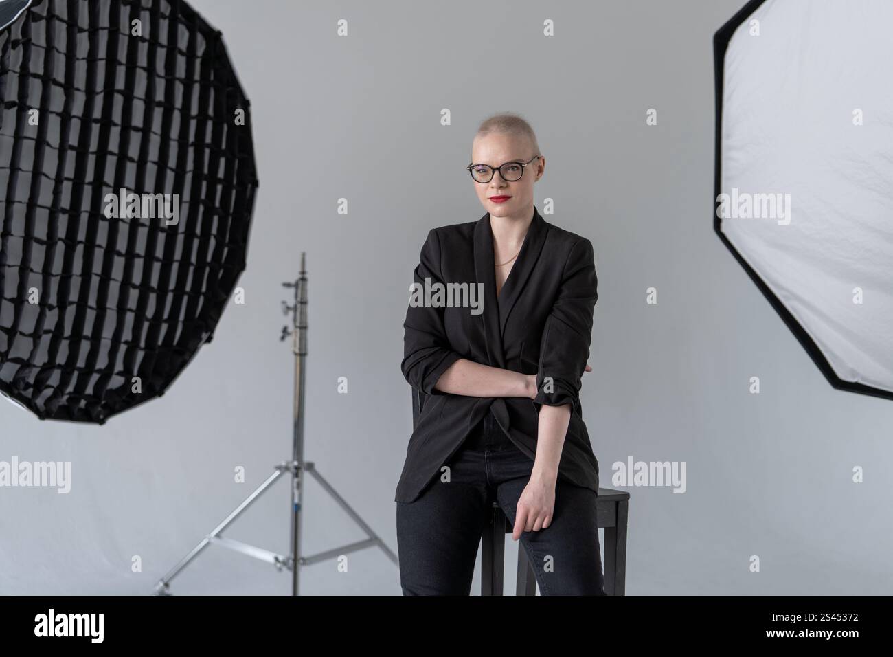 A professional woman poses confidently while seated in a photography studio with softbox lighting equipment, wearing formal business attire. Smiling W Stock Photo