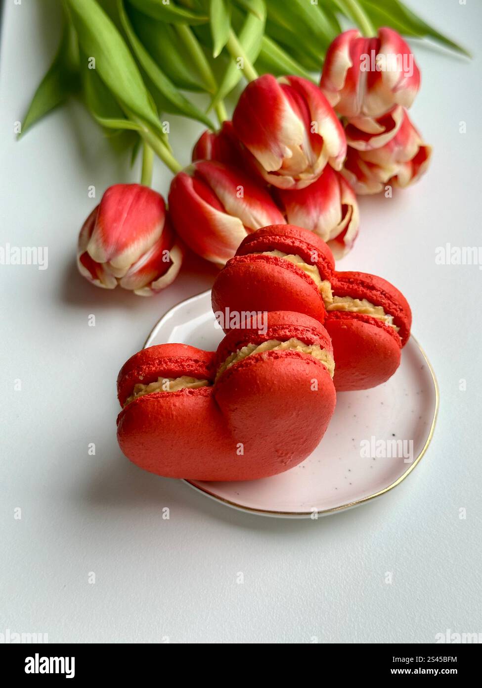 French dessert red hearts macarons on the white plate and red tulips on the white background - Smartphone Captured Stock Image