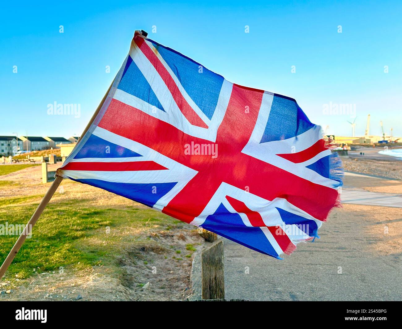 tattered union flag or union jack flying in the wind at blyth beach northumberland uk - Smartphone Captured Stock Image