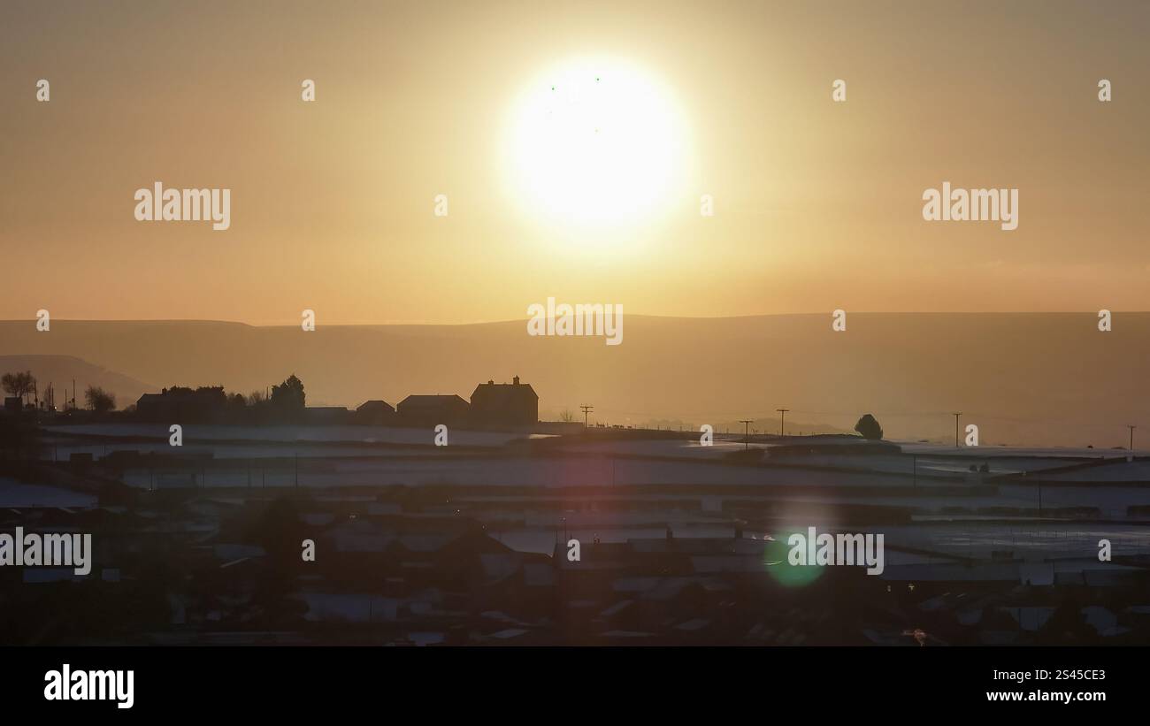 The sun sets over Emley Moor transmitting tower and the snow covered village of Emley as Sub-zero temperatures continue to hamper the north of the United Kingdom; Emley, Huddersfield, United Kingdom, 10th January 2025  (Photo by Mark Cosgrove/News Images) Stock Photo