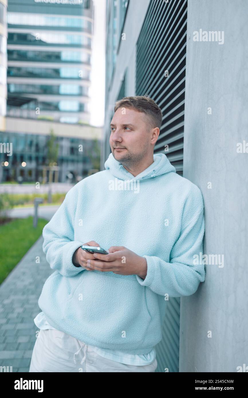 Successful young Caucasian man walking outside office building, engineer software developer programmer smiling and happy using test app on phone  Stock Photo