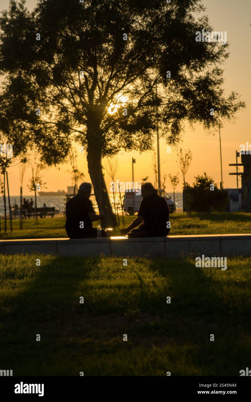 An elderly couple stands together at sunset, their silhouettes outlined by the warm, golden light. The peaceful moment captures love and companionship Stock Photo