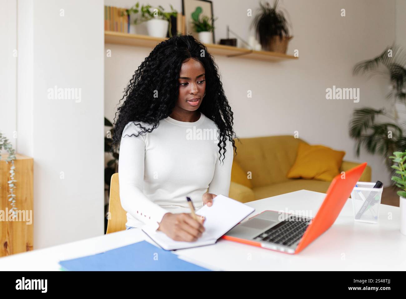 Focused young black woman taking notes while working remotely from home office Stock Photo