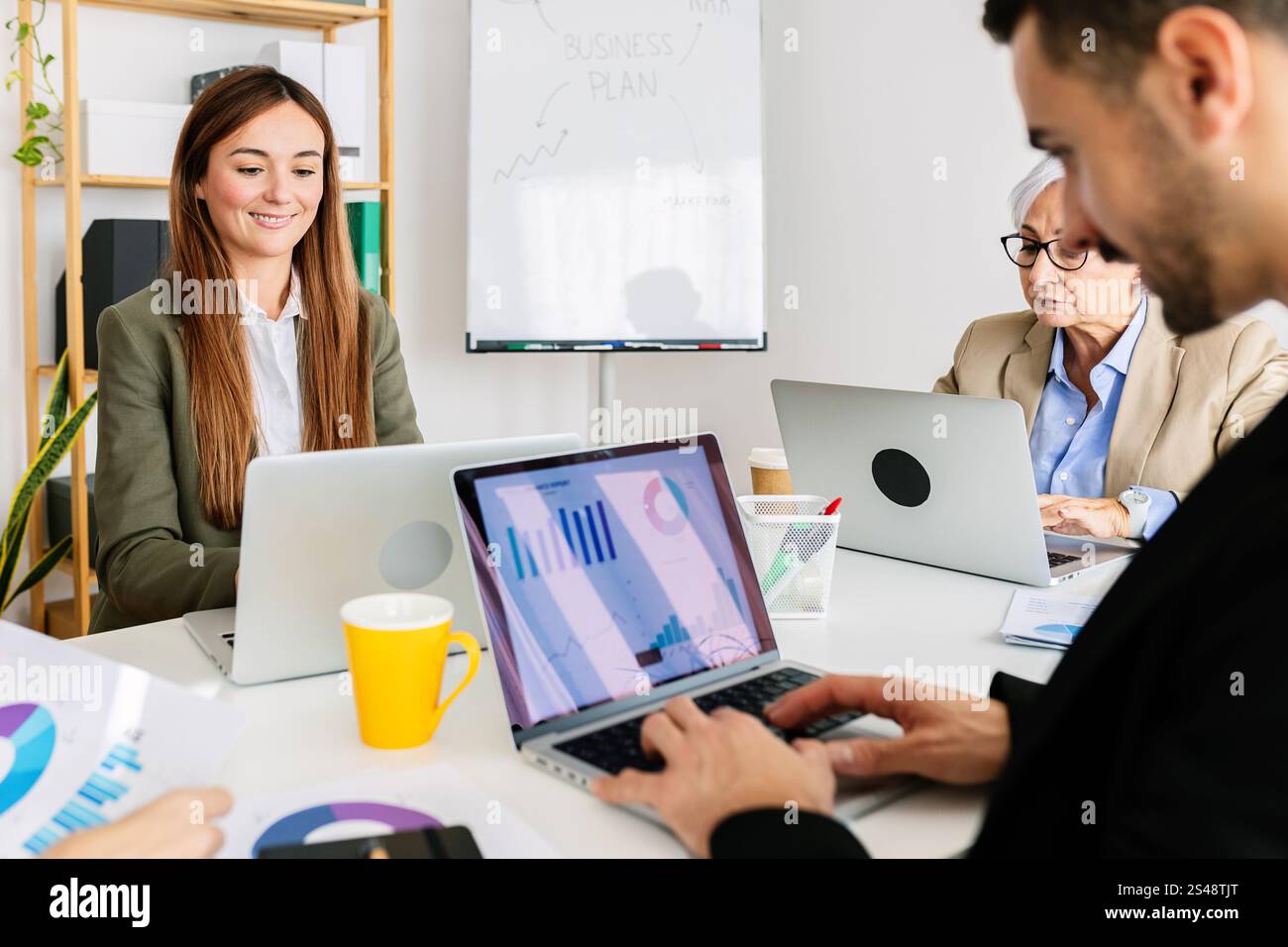 Business team analyzing charts and data on laptops in office meeting ...