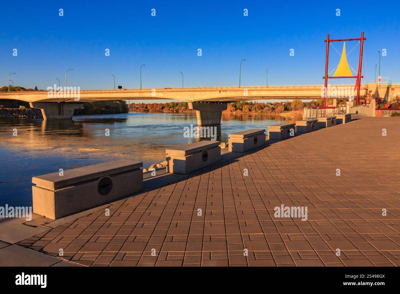 A bridge spans a river with a view of the water. The bridge is surrounded by a row of benches Stock Photo