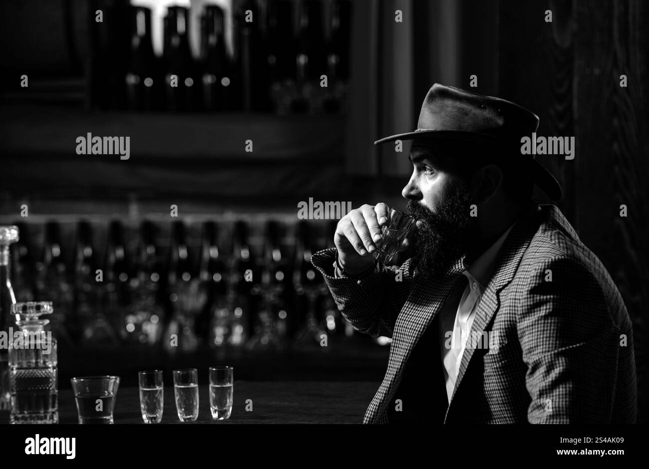 Confident bearded man in black suit with glass of whisky in loft. Stock Photo