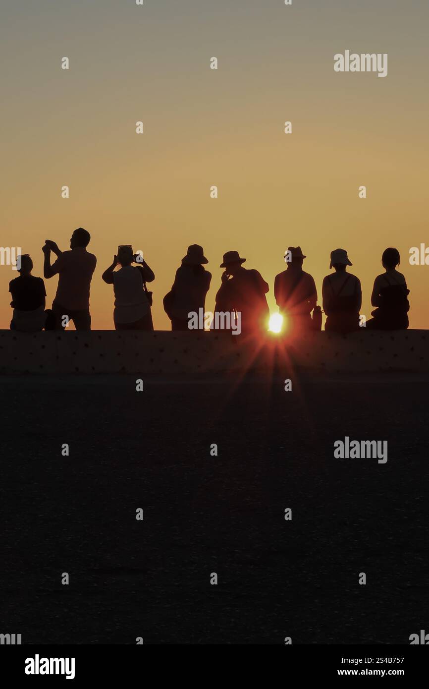 A group of people gathered on a ledge, their silhouettes backlit by a ...