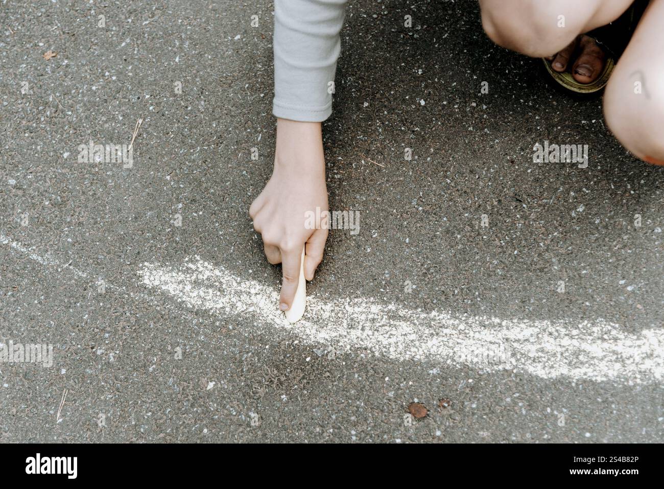 Child drawing with colored chalk on the asphalt, kid draw in ...