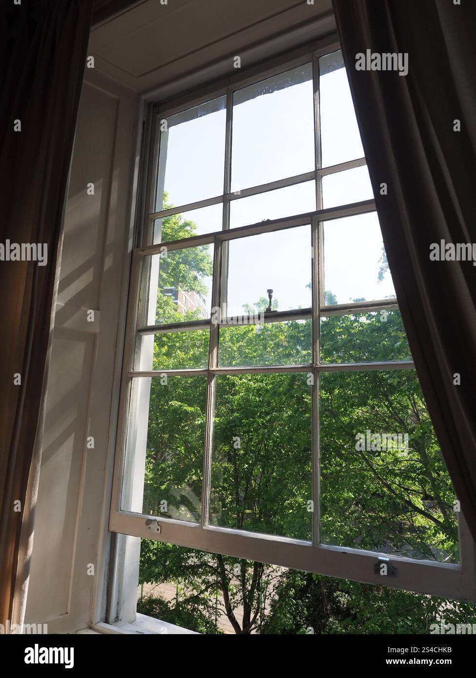 An old-fashioned wooden sash window partly open with a view out over ...