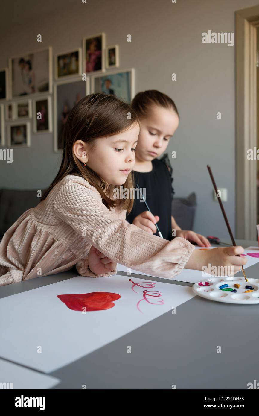 Two young girls painting together with watercolors in a home setting ...