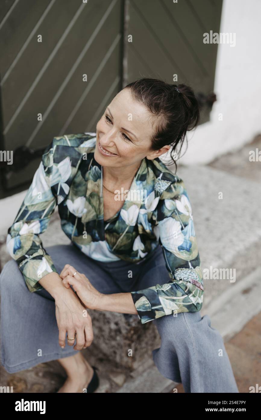 Smiling, dark-haired woman, 40+, sitting on a staircase Stock Photo