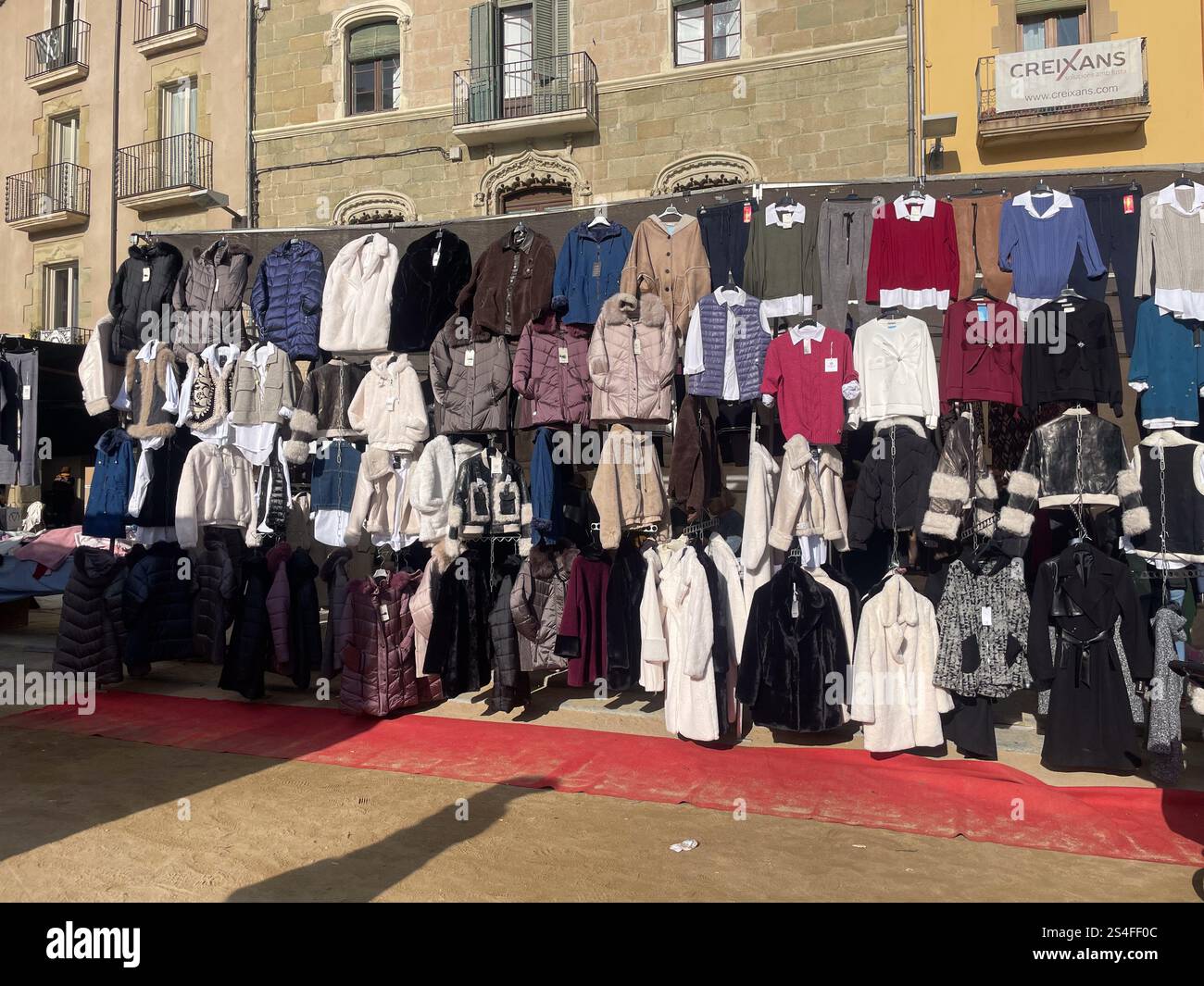 Display of various winter jackets, coats, and sweaters in different colors and styles at an outdoor market, street shopping, Vic, Catalonia, Spain - Smartphone Captured Stock Image