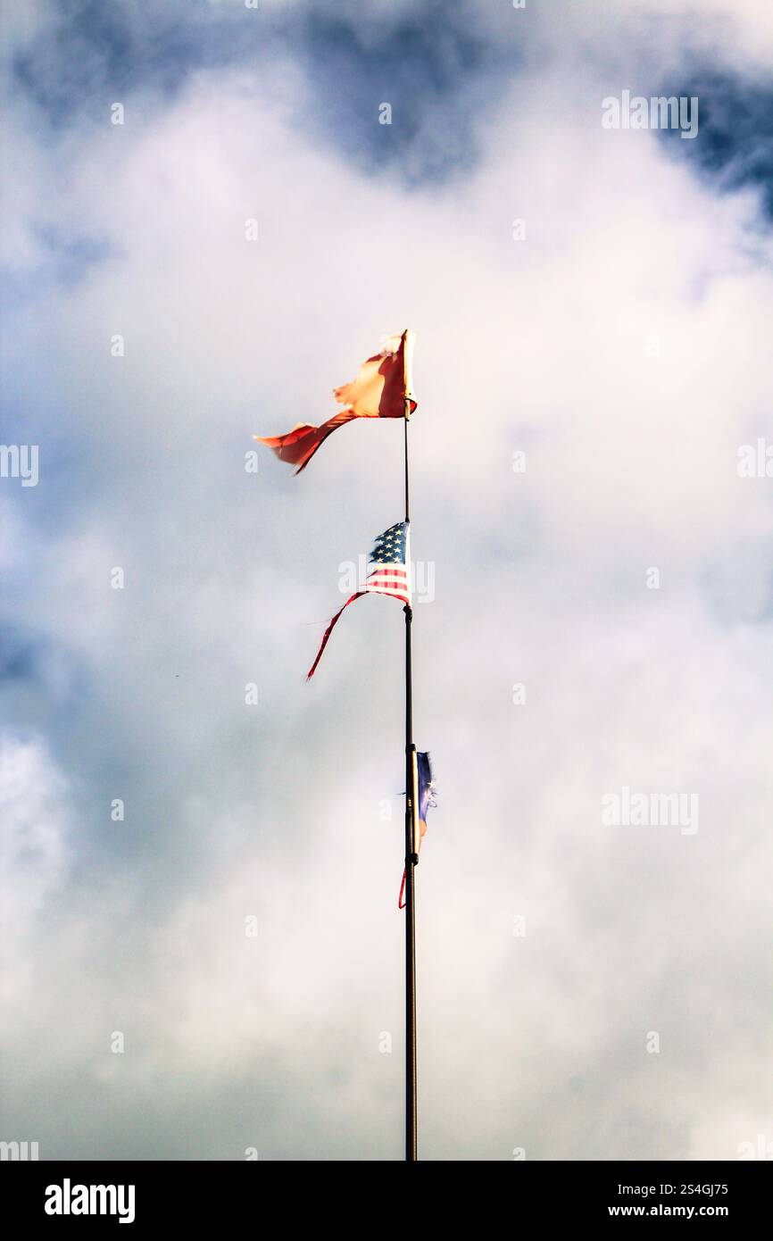 Zwei, einem Masten befestigte, Flaggen: Beide Flaggen sind zerfetzt. Die untere Flagge ist die amerikanische Nationalflagge 'Stars and Stripes'. Stock Photo