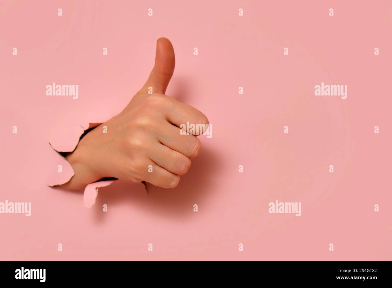 Hand showing thumbs up gesture through torn pink paper background ...