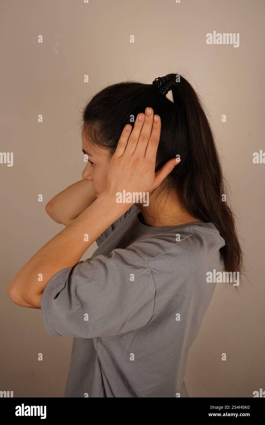 The person covers their ears with their palms, attempting to block out unwanted noise. This gesture conveys a desire to avoid unpleasant information Stock Photo