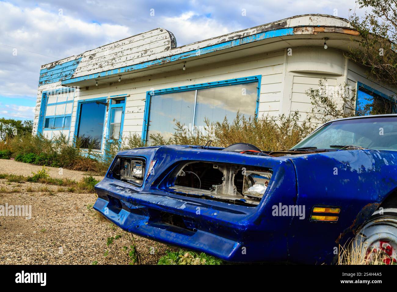 A blue car is parked in front of a white building. The car is old and ...