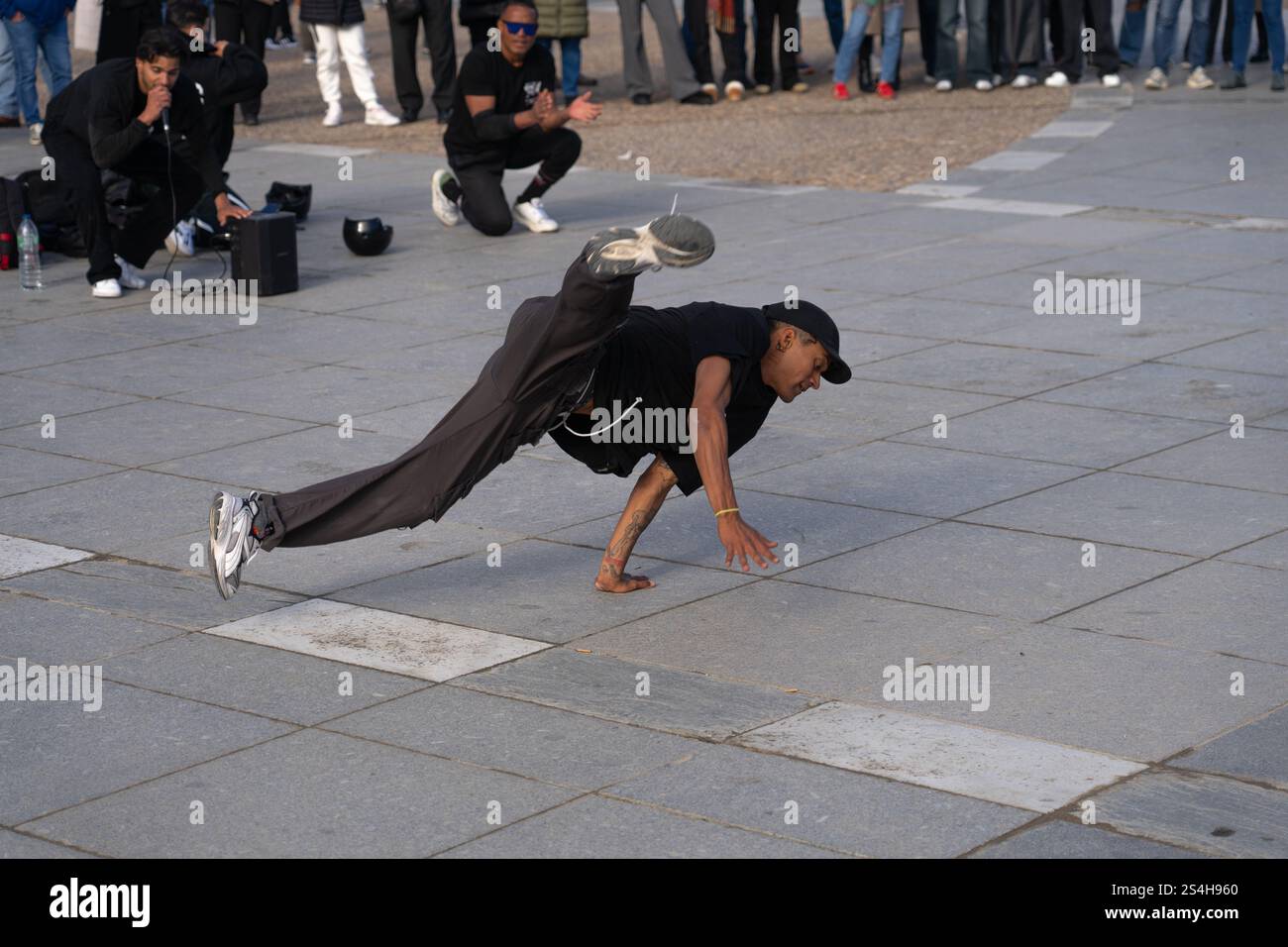Breakdancer performing an acrobatic move in the open air, in a crowded square, with an audience in the background cheering the performance. Stock Photo
