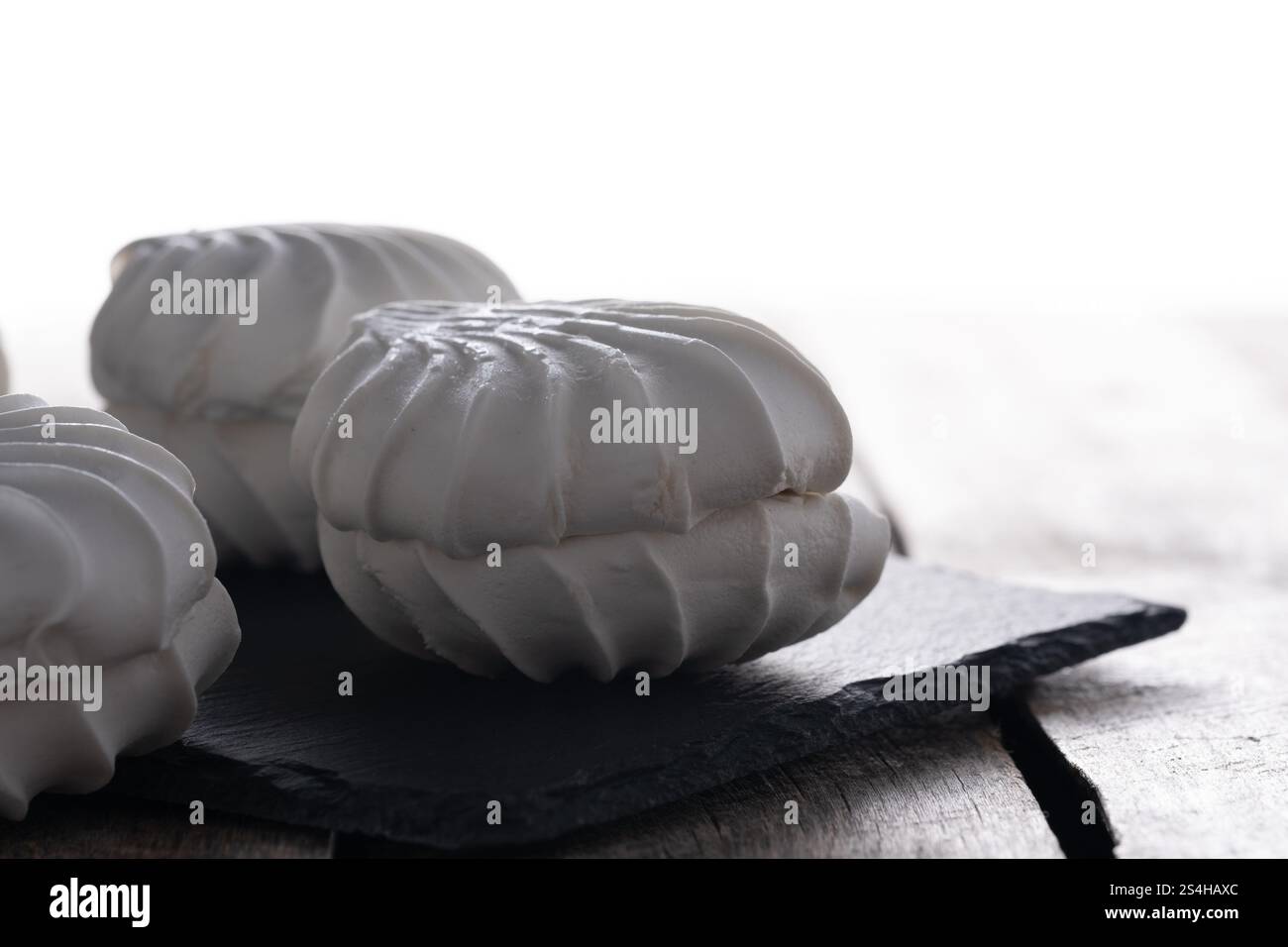 White marshmallows on black slate plate on white background Stock Photo