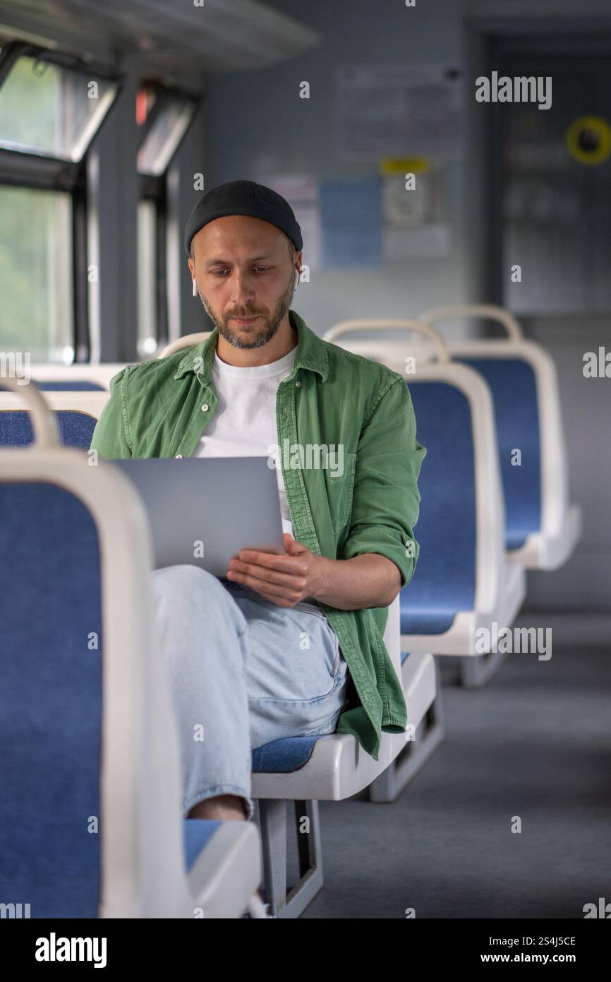 Focused thoughtful man passenger working on laptop while travel by electric train using earphones  Stock Photo