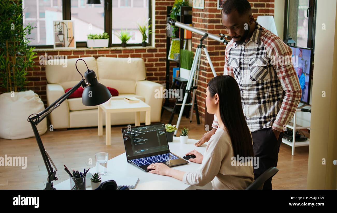Diverse software developers team coding on a laptop in a cozy home office, working on a new program or app development. Specialists in IT promote programming language and remote tech work. Camera A. Stock Photo