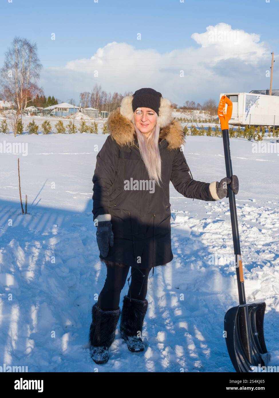 Woman wearing winter attire cheerfully clearing snow, enjoying bright ...