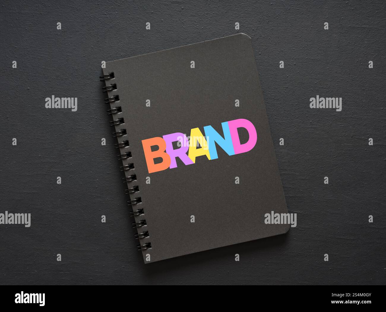 Colorful letters composing the word brand on a black notebook placed on a dark surface, representing branding strategy Stock Photo