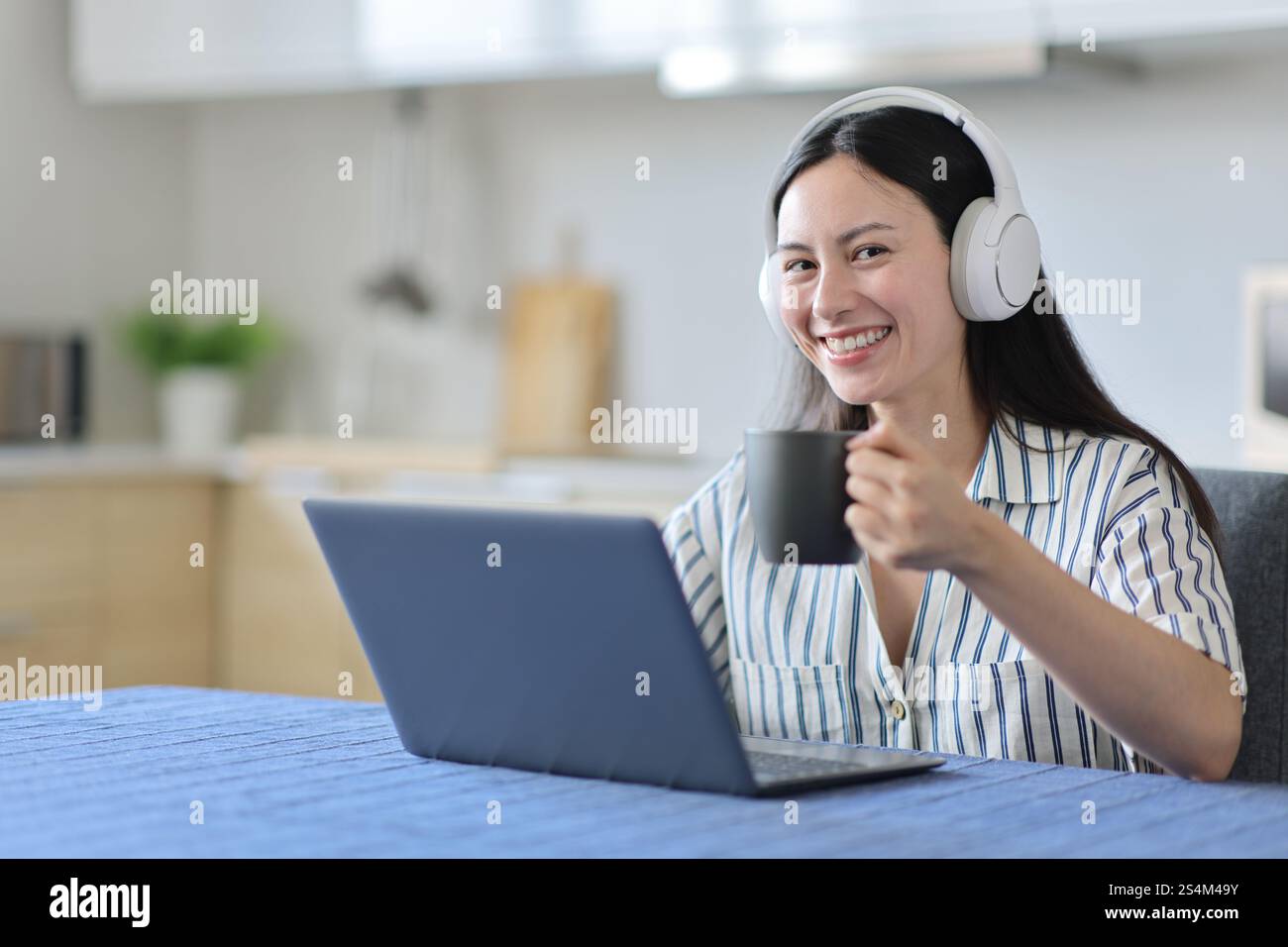 Happy asian woman using laptop and headphone drinking looks at you in ...