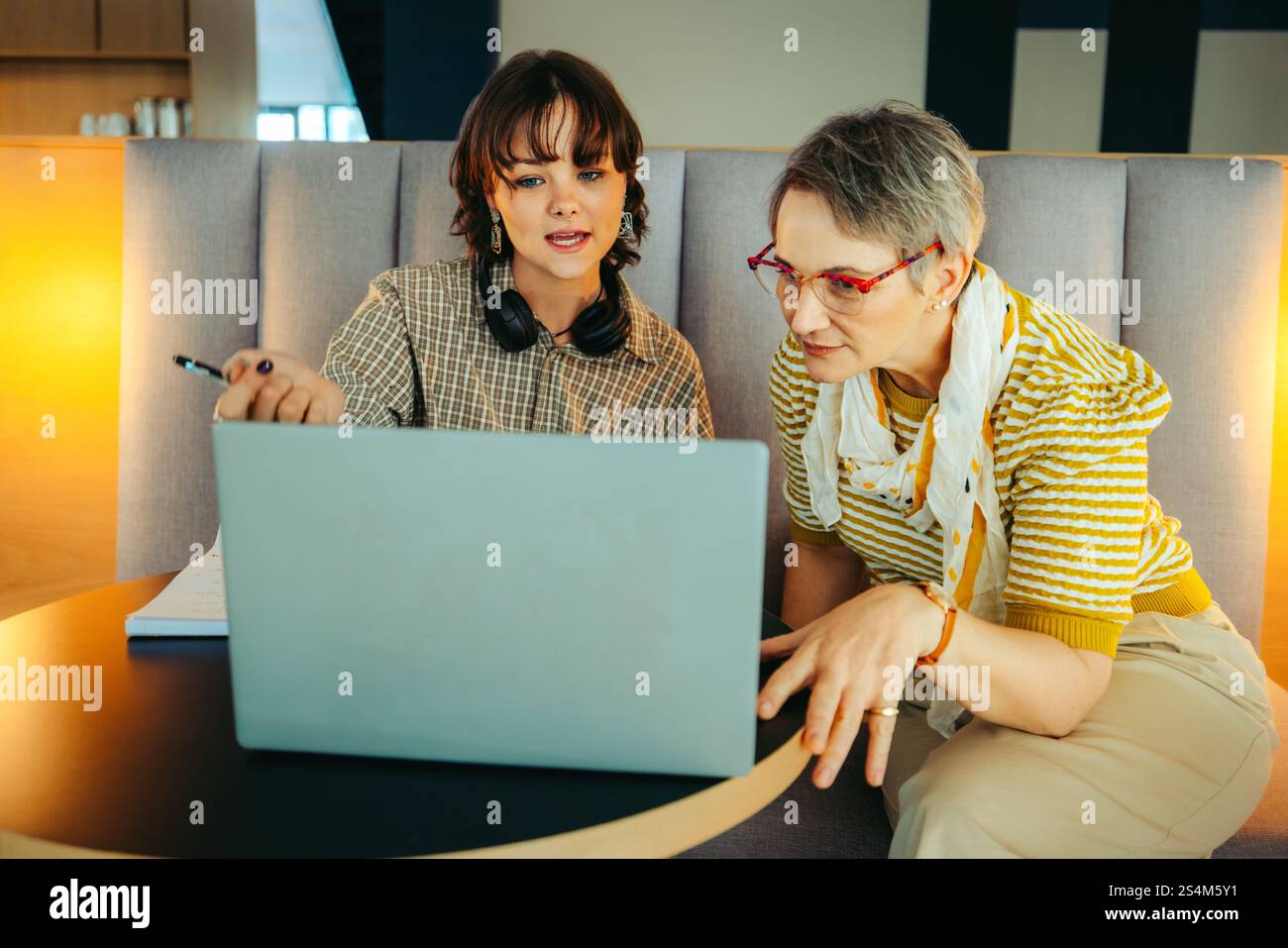 Two colleagues of different ages collaborating on a project using a laptop, showcasing diversity and teamwork in a professional environment. Stock Photo