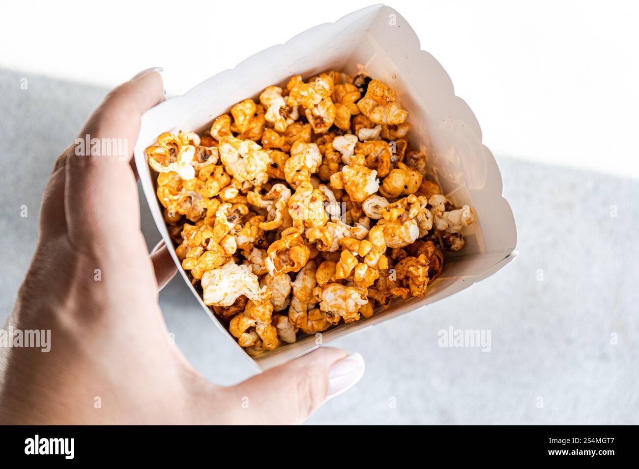 Cropped unrecognizable person in a close-up shot from above, holding a box filled with sweet caramel popcorn. Stock Photo