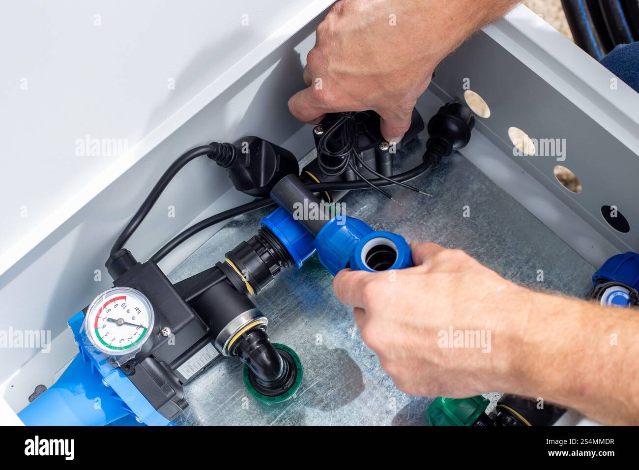 A man installs a drip irrigation system by placing an automatic valve in a metal box. Stock Photo