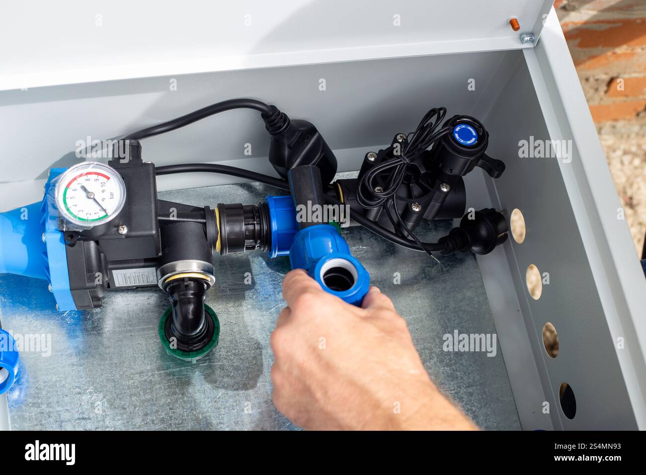 A man installs a drip irrigation system by placing a polypropylene compression tee into a metal box. Stock Photo