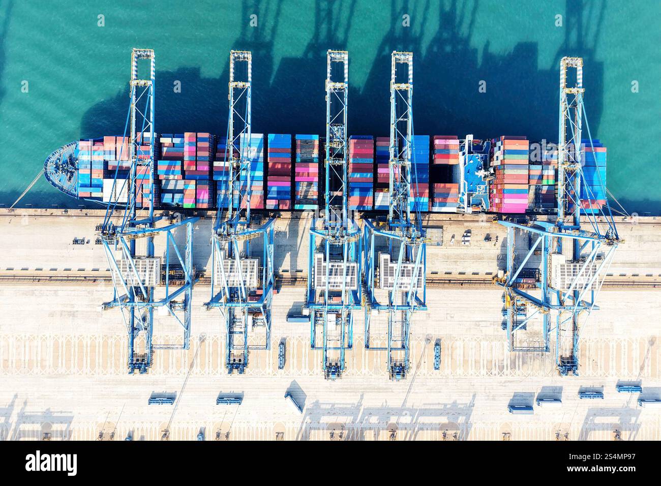 Quay cranes serve a container ship at a container terminal in Qingdao ...