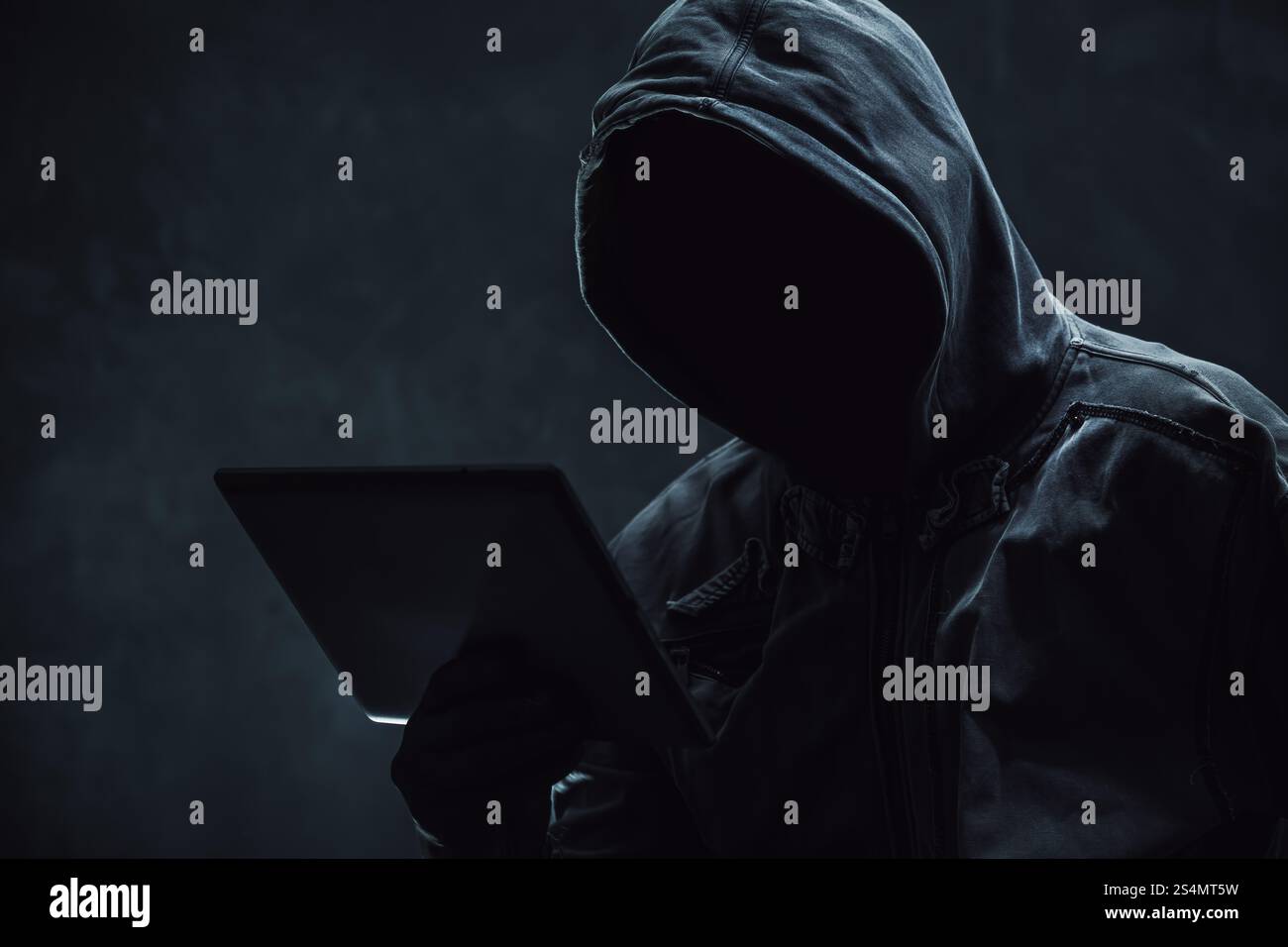 Hooded computer hacker using digital tablet, selective focus Stock Photo