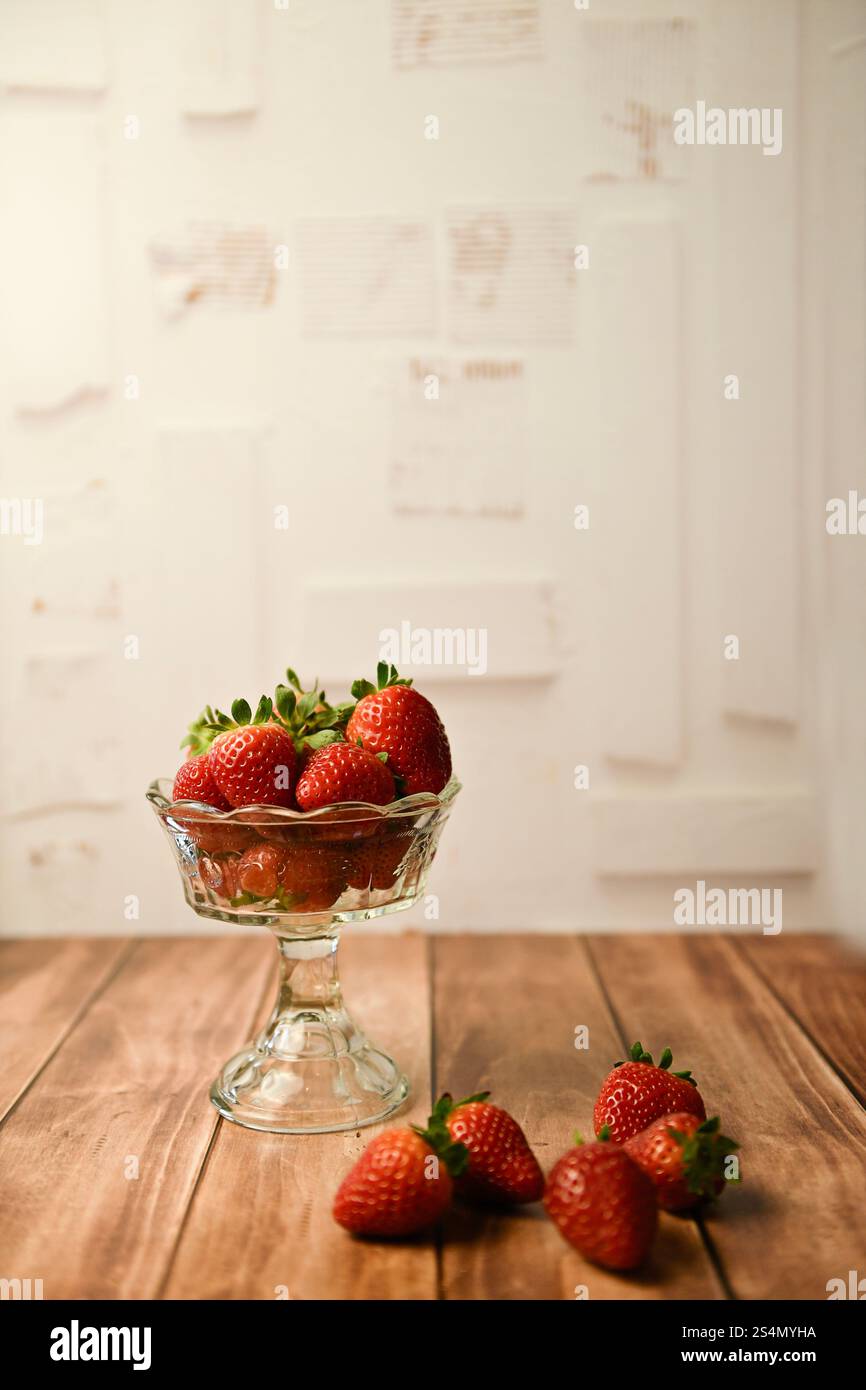 Fresh strawberries in a glass bowl on a wooden surface with a r Stock Photo