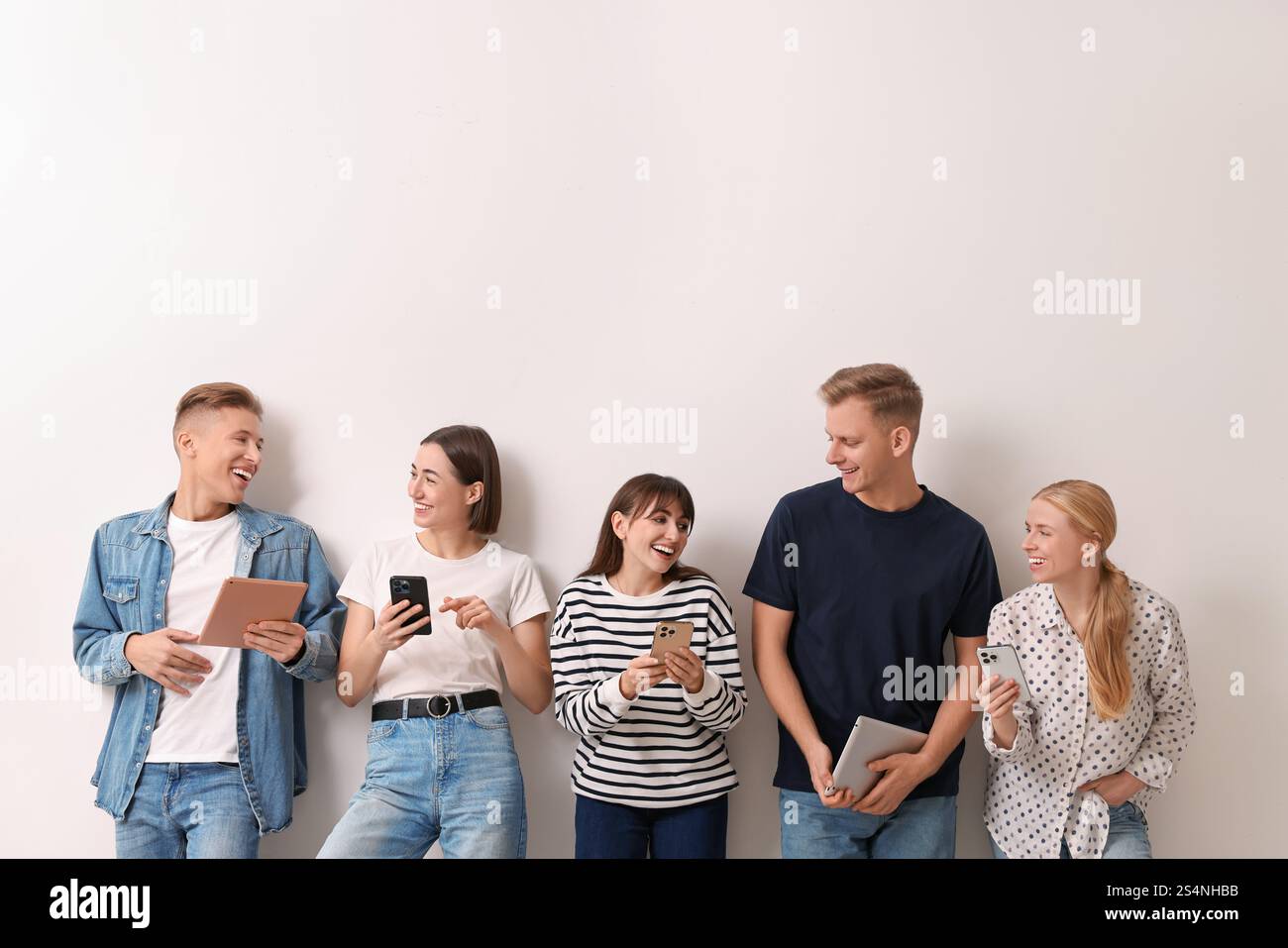 Group of people using different gadgets near white wall indoors. Modern ...
