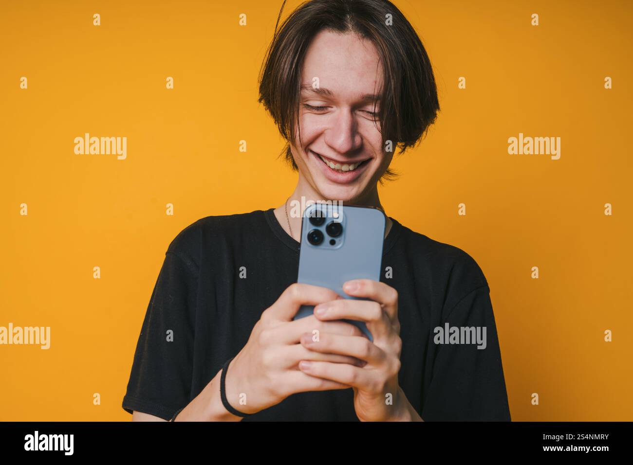 A Young Man Is Cheerfully Smiling While Using His Smartphone Against A Bright Yellow Background Stock Photo