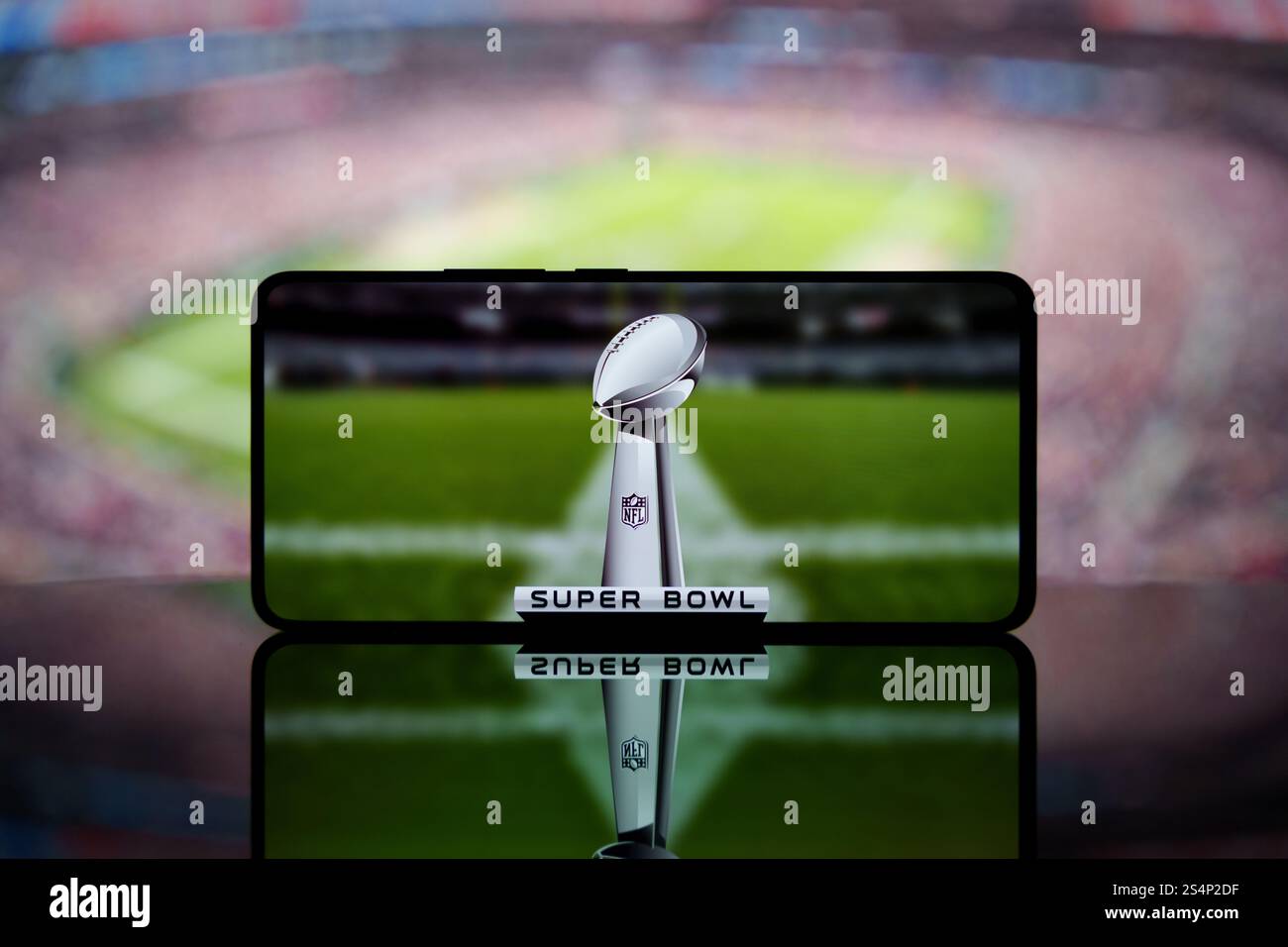 A smartphone displaying the Super Bowl trophy with a blurred American football stadium in the background. Stock Photo