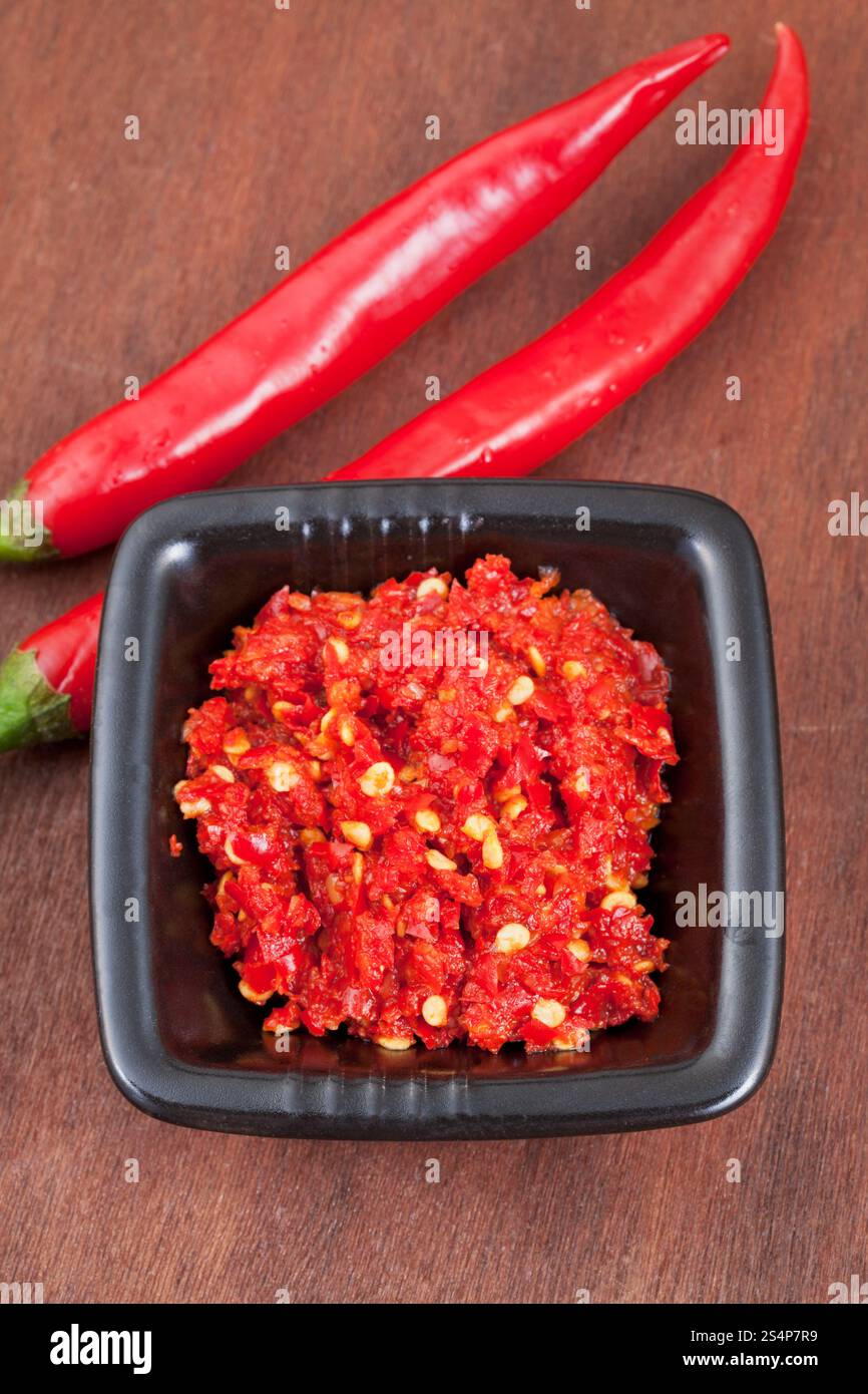 two pods of red hot pepper and spicy sauce on wooden table Stock Photo